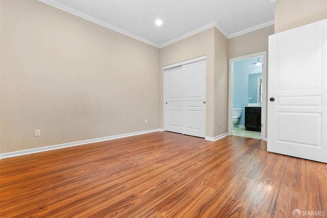 unfurnished bedroom featuring connected bathroom, baseboards, light wood-style floors, a closet, and crown molding