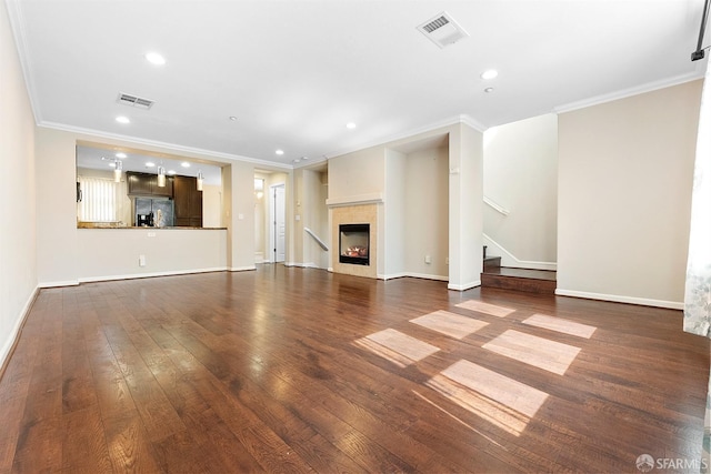 unfurnished living room with a warm lit fireplace, wood-type flooring, stairs, and visible vents