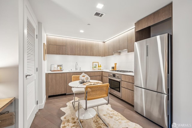 kitchen with sink, decorative backsplash, light brown cabinetry, wood-type flooring, and stainless steel appliances