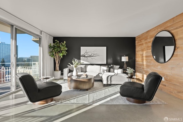 living room featuring an accent wall, wood walls, a skyline view, and concrete floors