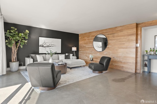 living area featuring an accent wall, wood walls, concrete floors, and baseboards