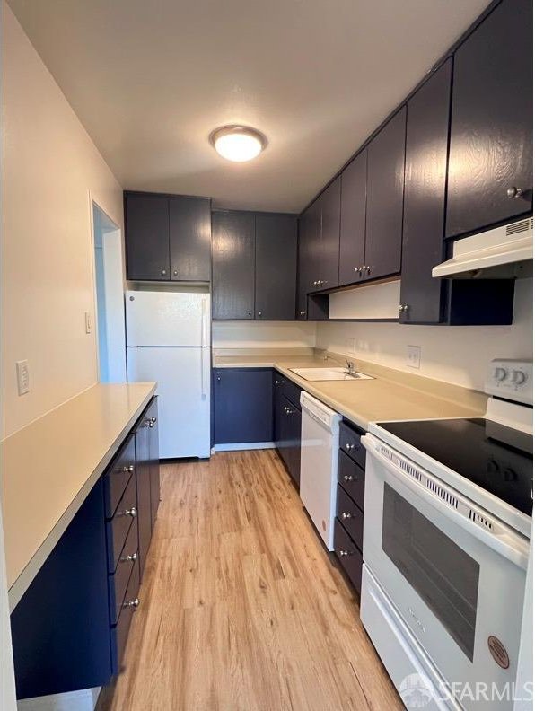 kitchen featuring light wood-type flooring, white appliances, sink, and range hood