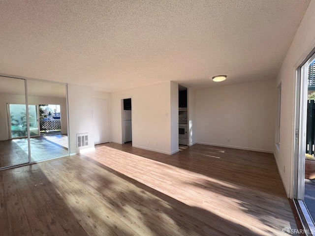 empty room featuring dark hardwood / wood-style floors, a textured ceiling, and a wealth of natural light