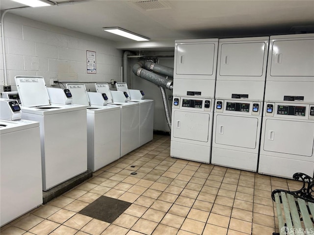 community laundry room with washing machine and dryer, stacked washer / drying machine, visible vents, and concrete block wall