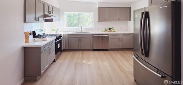 kitchen with lofted ceiling, sink, appliances with stainless steel finishes, and light hardwood / wood-style floors