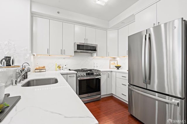 kitchen with stainless steel appliances, dark wood-style flooring, a sink, white cabinetry, and light stone countertops