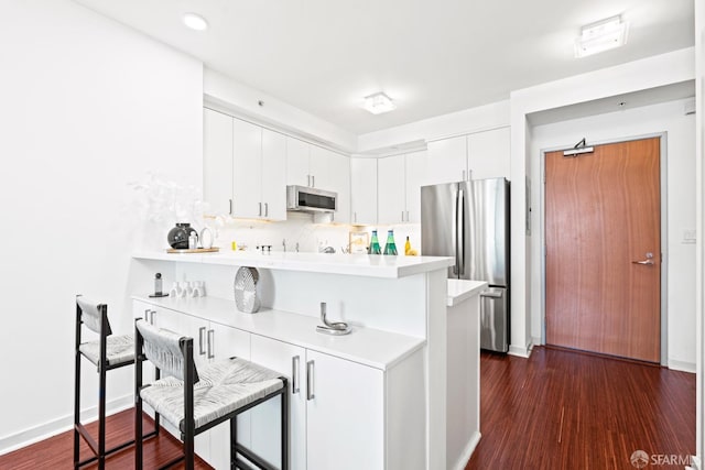 kitchen featuring a peninsula, dark wood-style flooring, stainless steel appliances, and light countertops