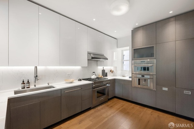 kitchen with a sink, wall chimney exhaust hood, appliances with stainless steel finishes, modern cabinets, and light wood finished floors