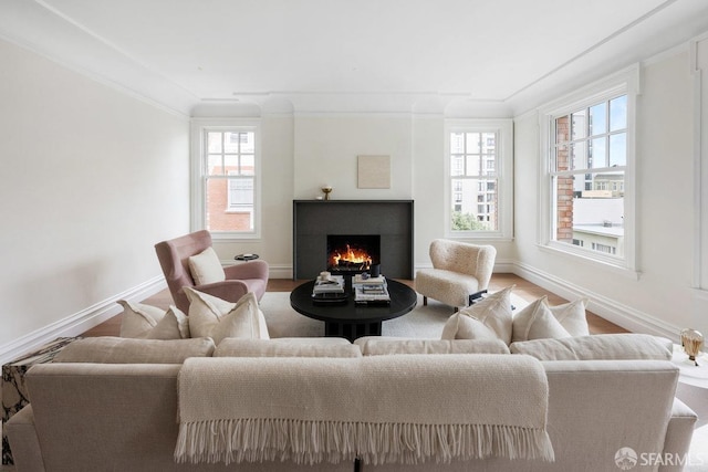 living room featuring baseboards, plenty of natural light, a lit fireplace, and crown molding