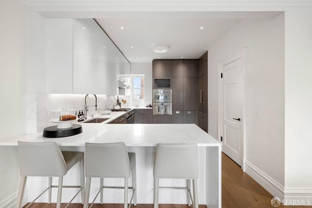 kitchen featuring a sink, modern cabinets, backsplash, a peninsula, and a breakfast bar