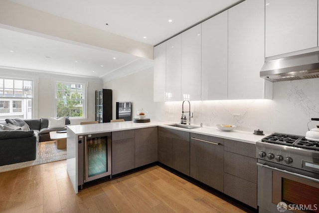kitchen with a sink, stainless steel gas range, beverage cooler, modern cabinets, and a peninsula