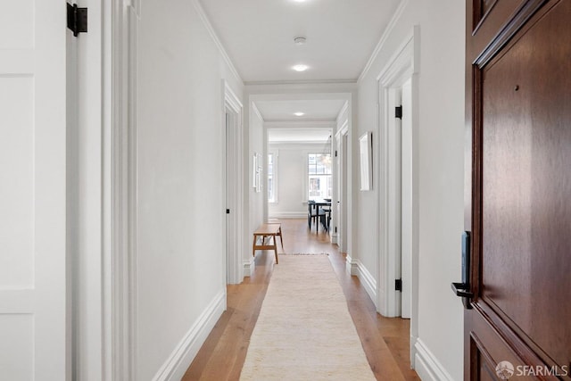 hallway with light wood-style flooring, baseboards, and crown molding