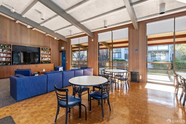 dining area with wood walls, beamed ceiling, a textured ceiling, and parquet flooring