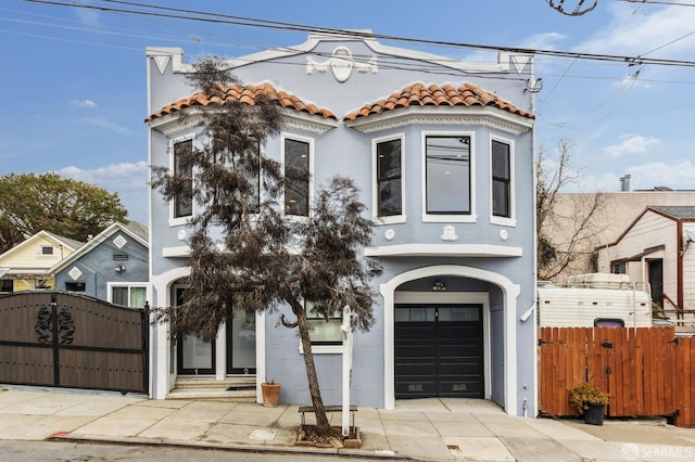 mediterranean / spanish-style home featuring concrete driveway, a tiled roof, an attached garage, a gate, and fence