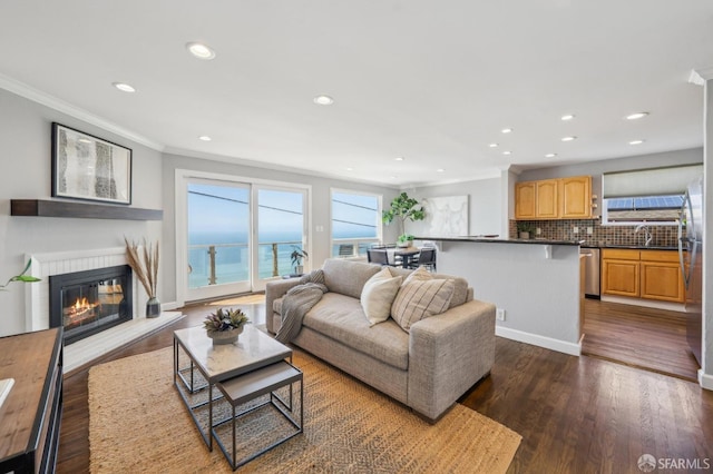 living room featuring recessed lighting, dark wood-style floors, a glass covered fireplace, and crown molding