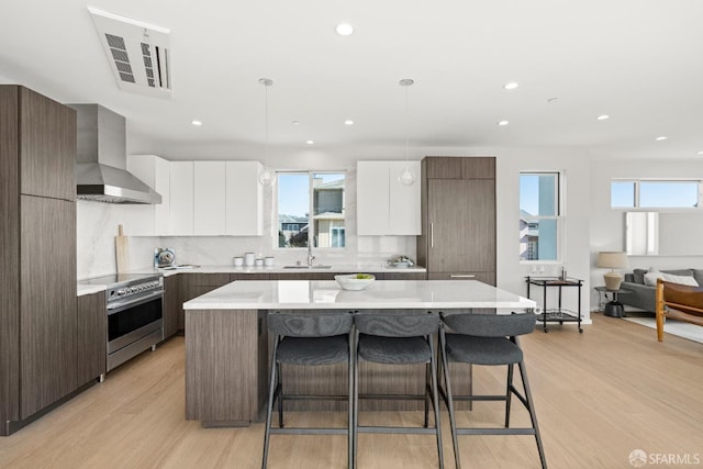 kitchen with a center island, wall chimney exhaust hood, stainless steel range, and white cabinets