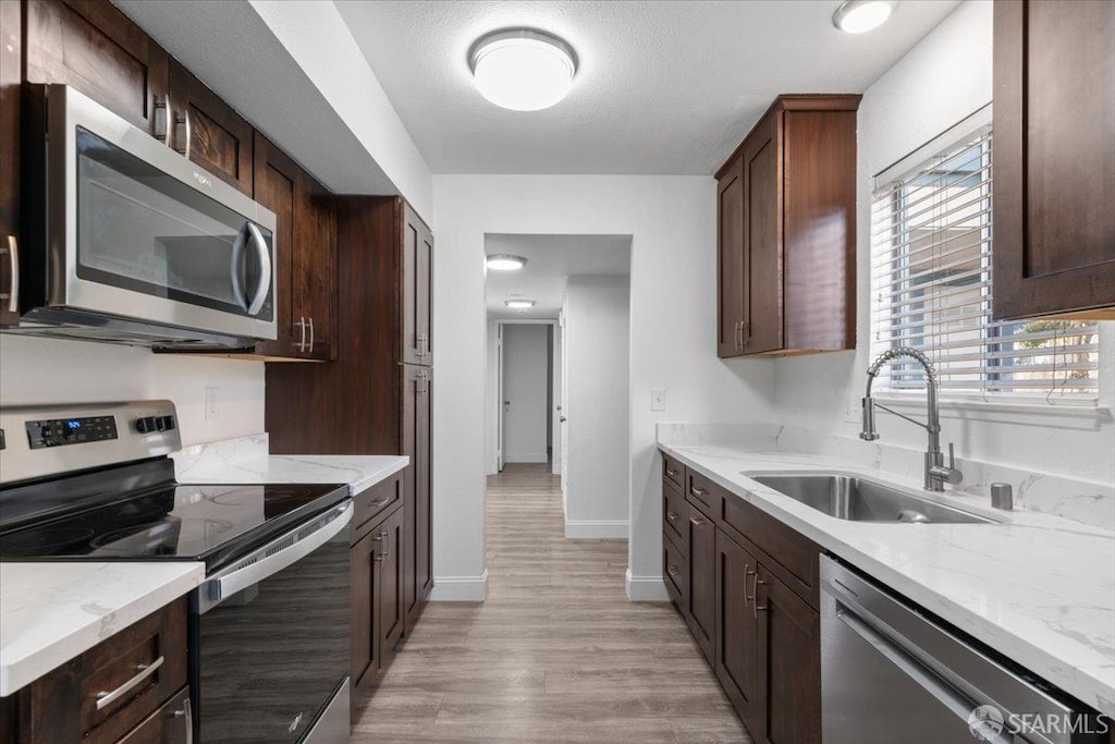 kitchen featuring sink, dark brown cabinetry, stainless steel appliances, light stone countertops, and light wood-type flooring