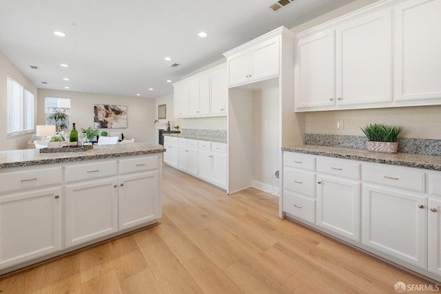 kitchen with white cabinetry, light stone counters, and light hardwood / wood-style flooring