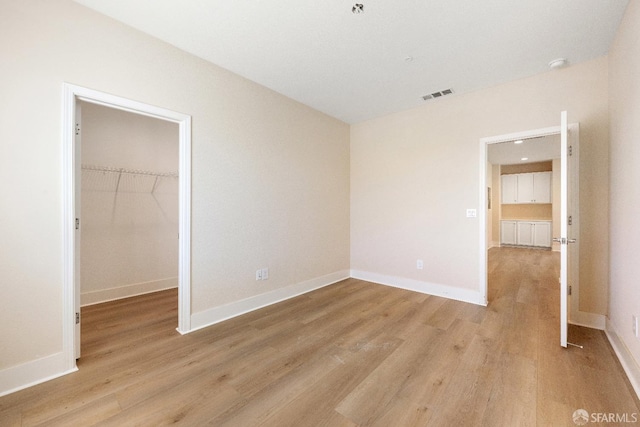 unfurnished bedroom featuring a walk in closet, light hardwood / wood-style flooring, and a closet