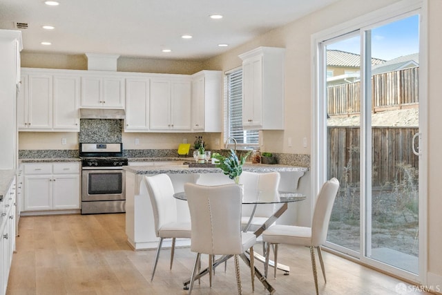 kitchen with light stone counters, light hardwood / wood-style floors, a breakfast bar area, white cabinets, and stainless steel range with gas stovetop