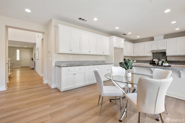 kitchen with dark stone counters, light hardwood / wood-style floors, decorative backsplash, and white cabinetry