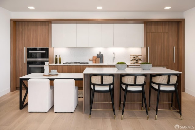 kitchen with white cabinetry, a kitchen island, a breakfast bar area, and double wall oven