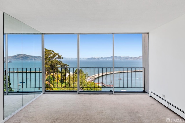 carpeted empty room with floor to ceiling windows, a water and mountain view, a baseboard heating unit, and plenty of natural light