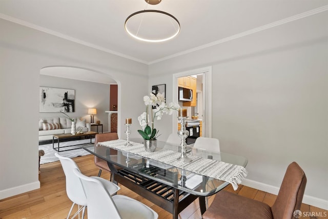 dining space with arched walkways, light wood finished floors, crown molding, and baseboards