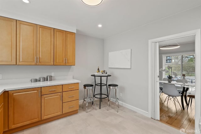 kitchen featuring baseboards, light countertops, recessed lighting, and brown cabinetry