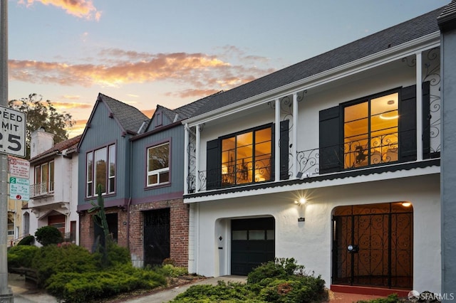 multi unit property with a balcony, a garage, stucco siding, and brick siding