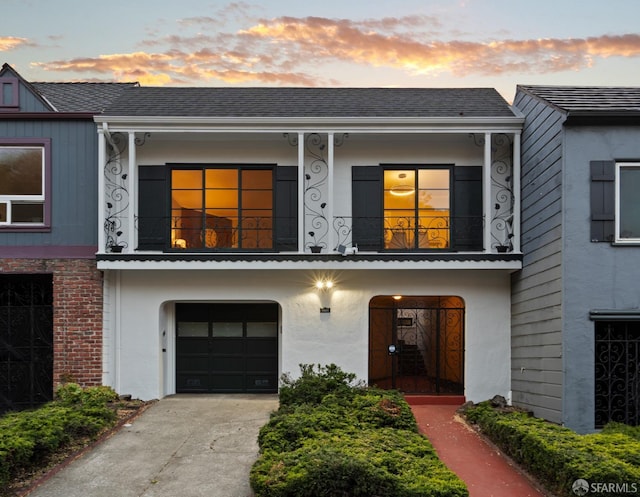 multi unit property featuring a balcony, an attached garage, driveway, and roof with shingles