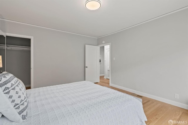 bedroom featuring wood finished floors, baseboards, a closet, and ornamental molding