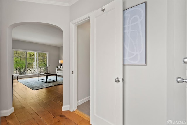 hall featuring arched walkways, hardwood / wood-style flooring, baseboards, and crown molding