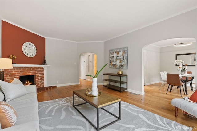 living room featuring arched walkways, wood-type flooring, crown molding, baseboards, and a brick fireplace