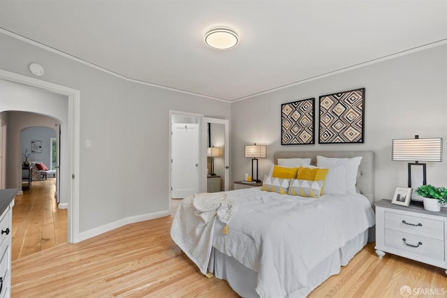 bedroom featuring arched walkways, light wood-type flooring, baseboards, and ornamental molding