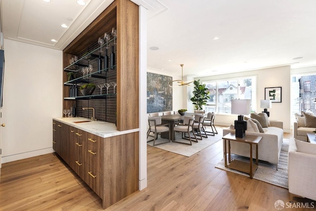 bar featuring sink, a notable chandelier, light hardwood / wood-style floors, ornamental molding, and dark brown cabinetry