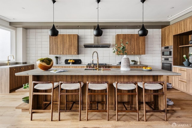 kitchen with hanging light fixtures, a kitchen island with sink, stainless steel double oven, and tasteful backsplash