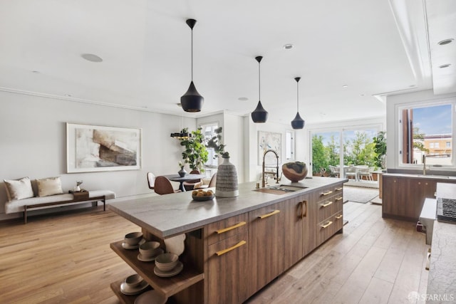 kitchen with light wood-style flooring, a sink, dark countertops, modern cabinets, and a center island with sink