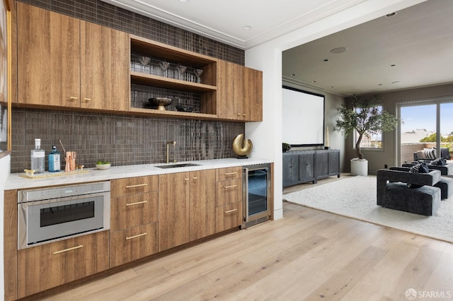 kitchen with beverage cooler, wall oven, light wood-type flooring, sink, and tasteful backsplash