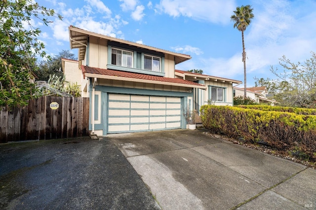 view of front of house with stucco siding, driveway, an attached garage, and fence