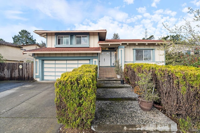 tri-level home with concrete driveway, a tiled roof, fence, and a garage