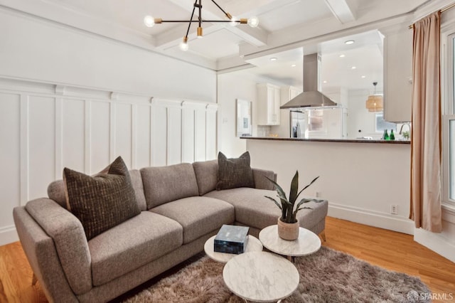 living room featuring coffered ceiling, crown molding, a notable chandelier, beam ceiling, and light hardwood / wood-style flooring