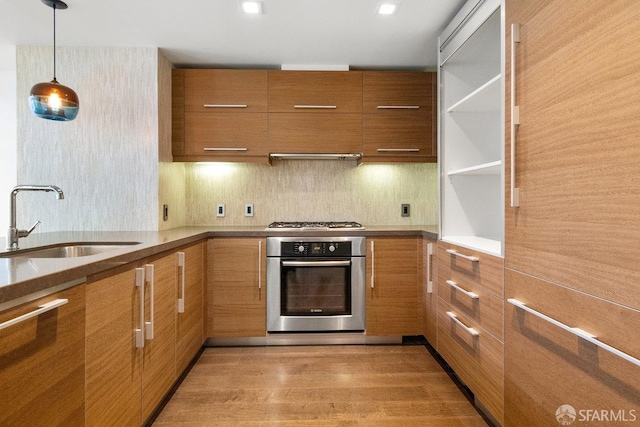 kitchen featuring pendant lighting, sink, backsplash, hardwood / wood-style flooring, and stainless steel appliances