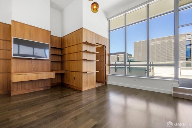 unfurnished living room featuring a towering ceiling, dark wood-type flooring, and wood walls