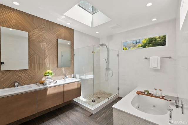 full bathroom with a skylight, a shower stall, a jetted tub, double vanity, and recessed lighting