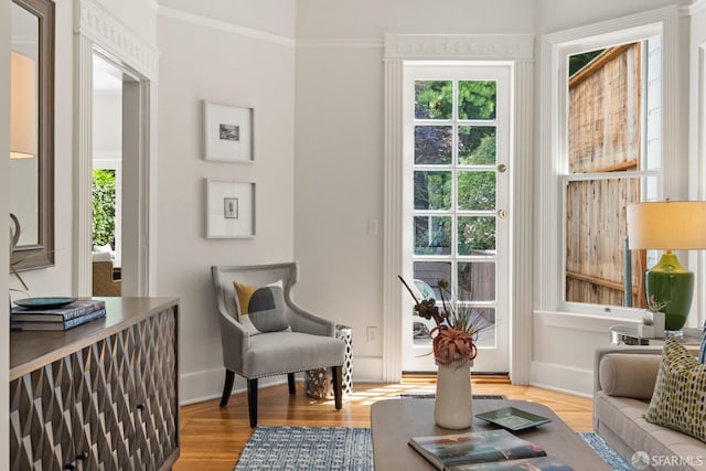 living area with healthy amount of natural light, wood finished floors, crown molding, and baseboards