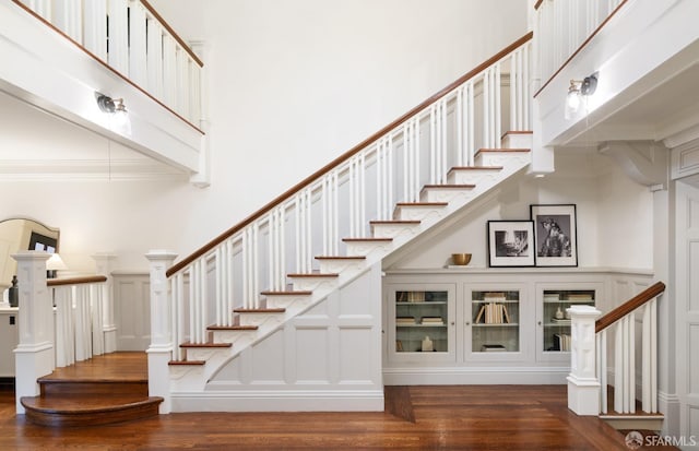 stairway with hardwood / wood-style flooring, a towering ceiling, and crown molding