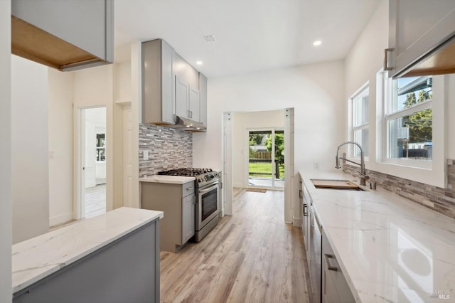 kitchen with light wood-type flooring, sink, stainless steel gas range oven, gray cabinets, and light stone countertops