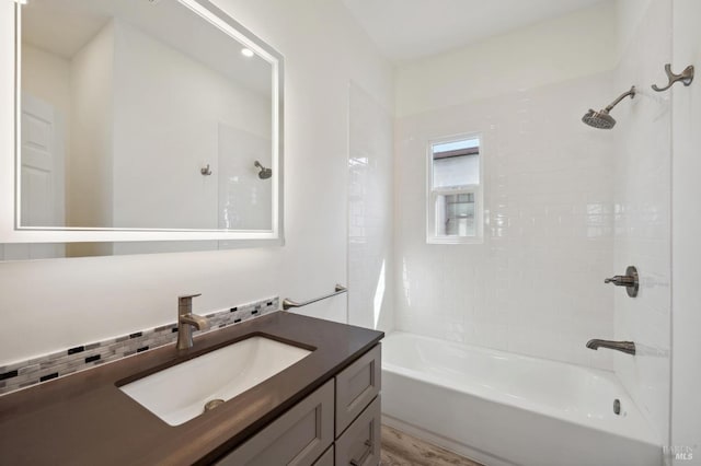 bathroom featuring vanity, hardwood / wood-style floors, tiled shower / bath, and tasteful backsplash