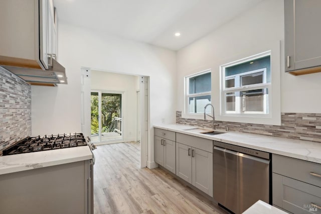 kitchen with sink, tasteful backsplash, gray cabinetry, stainless steel dishwasher, and light hardwood / wood-style flooring